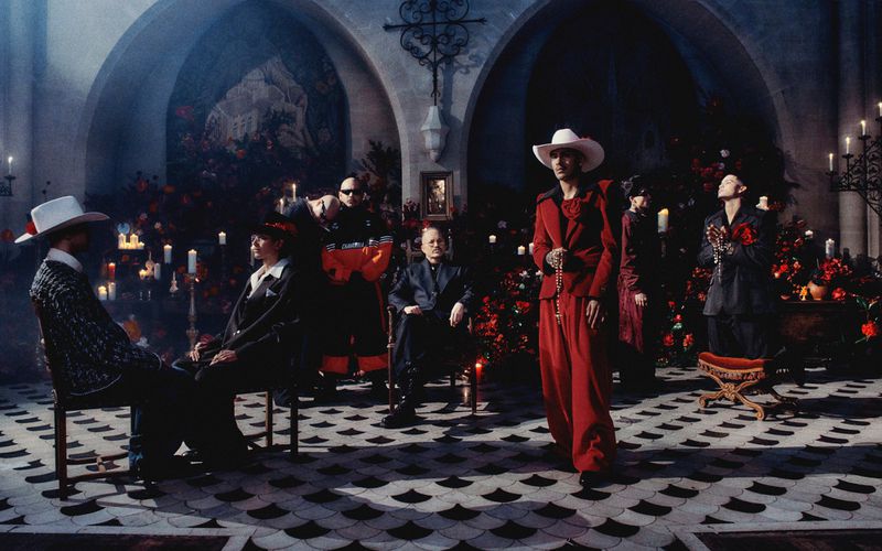 Fashionable group in a church setting: A man in red stands out amidst the candlelit ambiance and floral decorations, capturing a formal gathering.
