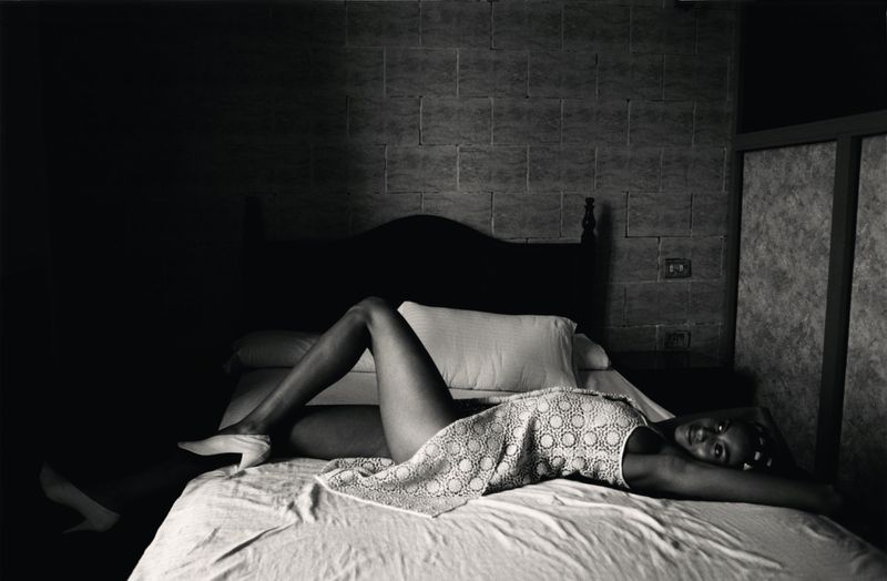 Imaan Hammam lying on a bed wearing a patterned dress in a low-light interior photographed by Vincent van de Wijngaard for M Le magazine du Monde.