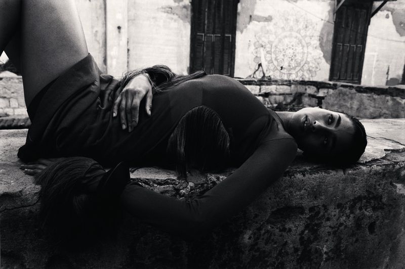 Monochrome shot of a woman reclining on a stone surface in an outdoor setting, showcasing fashion and portraiture with an editorial style.