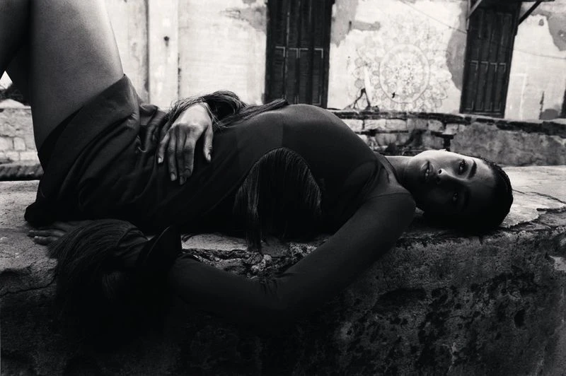 Monochrome shot of a woman reclining on a stone surface in an outdoor setting, showcasing fashion and portraiture with an editorial style.