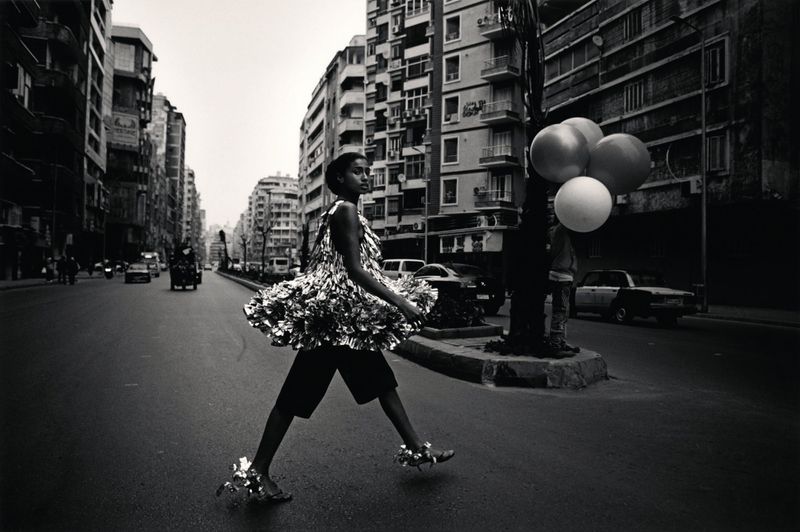 Woman in a silver dress walks down a city street with balloons in a black and white photograph, urban fashion, street style, city fashion.