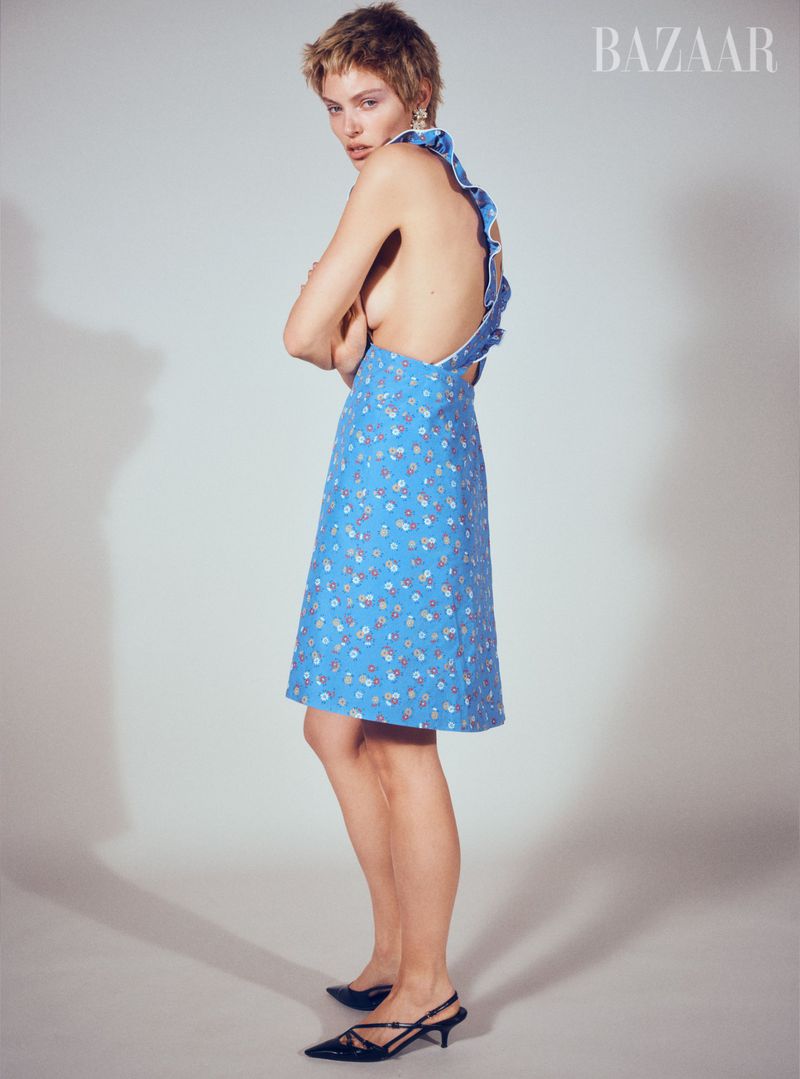 Adult female fashion model with short hair wearing a blue floral dress and black slingback heels in a photo studio.