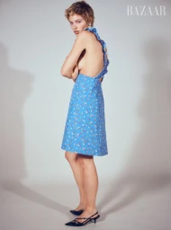 Model wearing a blue ruffled floral dress and black slingback heels standing against a neutral studio background.