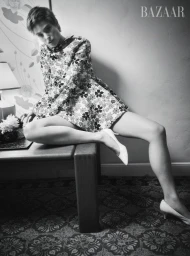 Model Bibi Breslin in a patterned mini dress and white heels seated on a table for Harper's Bazaar U.S.