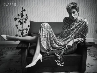 Model Bibi Breslin seated in an armchair holding flowers for Harper's Bazaar U.S., photographed by Josh Olins.