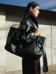 Profile of a woman wearing a black leather jacket carrying a large black leather tote bag outside a building with metal shutters.