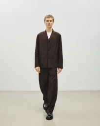 Male model wearing a dark brown suit jacket and matching trousers against a white seamless studio backdrop.