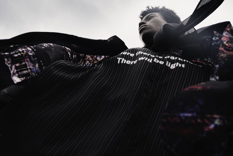 Portrait of a young adult male of African descent, styled in black and white shirt, with the text 'There will be light'.