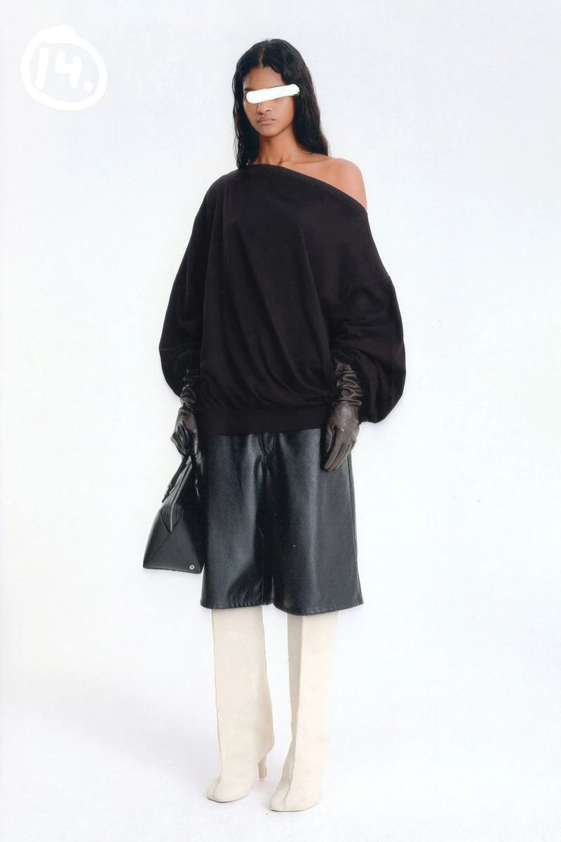 Woman in black off-the-shoulder top, leather shorts, gloves, and cream boots against a white background in a fashion editorial.