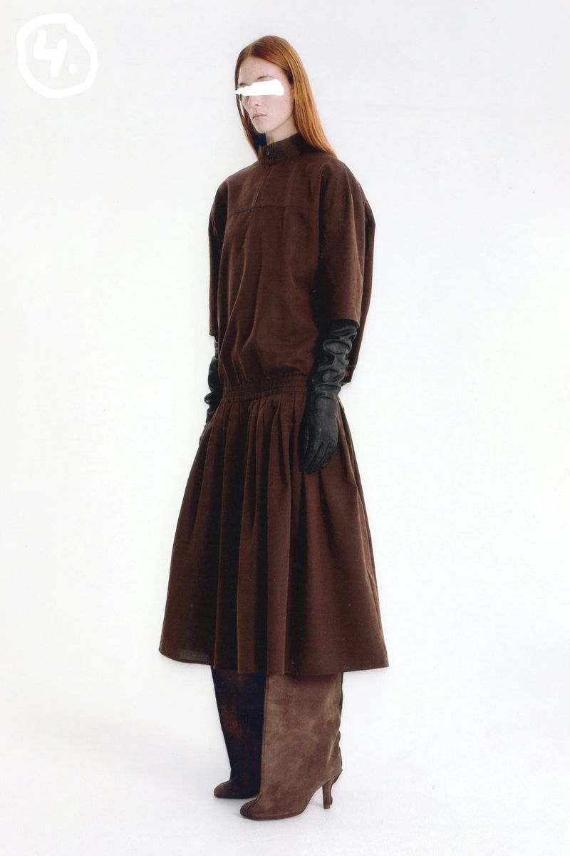 Model standing against a white backdrop wearing a brown dress and long black leather gloves