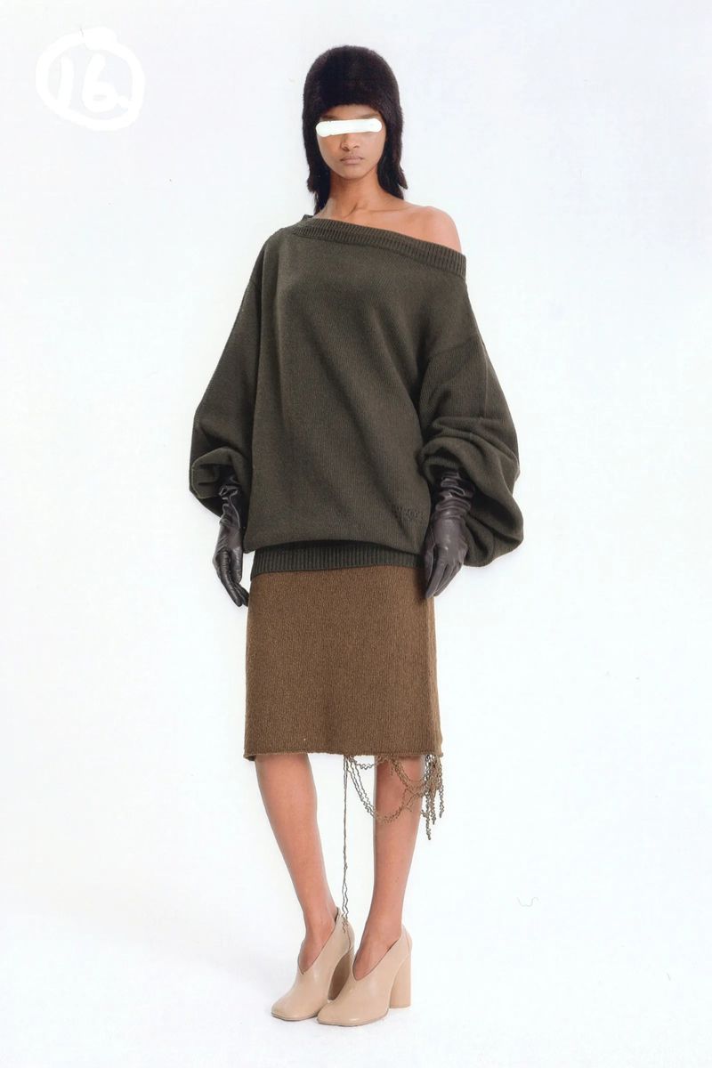 Full-body shot of a woman wearing an olive sweater, brown skirt with fringe, black gloves, a fur cap, and high-heeled shoes.