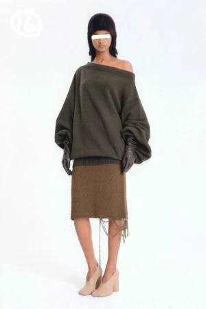 Full-body shot of a woman wearing an olive sweater, brown skirt with fringe, black gloves, a fur cap, and high-heeled shoes.