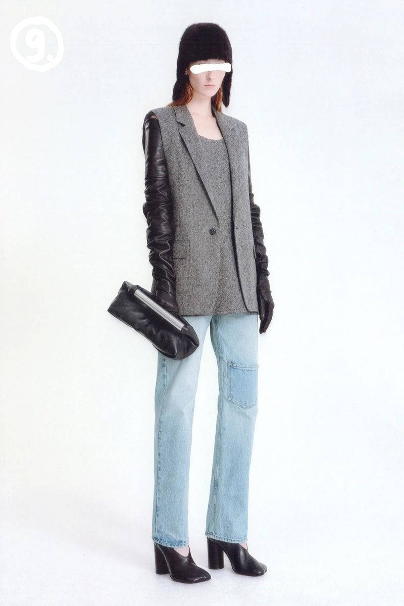 Fashionable woman in light-wash jeans, grey blazer, and black leather accessories poses against a bright white backdrop in a studio shot.