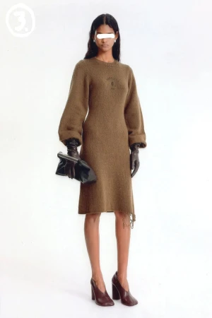 Model wearing a brown knit dress, dark gloves, and high heels, holding a black clutch against a white seamless backdrop.