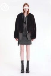 Model wearing a dark fur jacket over grey layers and a skirt against a plain white background
