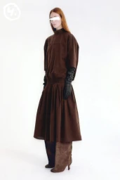 Model standing against a white backdrop wearing a brown dress and long black leather gloves