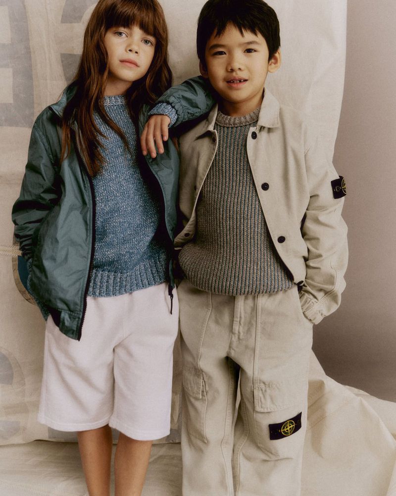 Two children, a boy and a girl, wearing casual outerwear, pose indoors against a neutral backdrop, showcasing youth fashion.