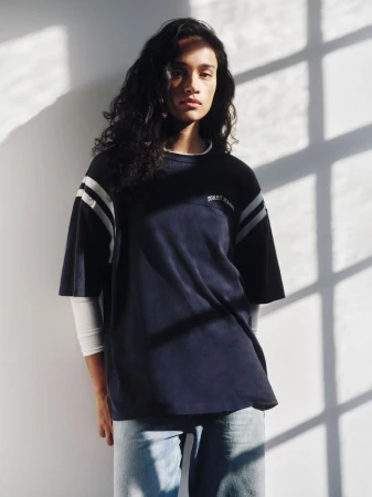 Model wearing dark t-shirt and light denim jeans against wall with window shadows for Tommy Jeans