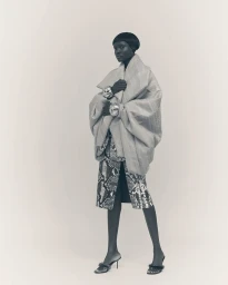 Model wearing a voluminous quilted wrap jacket and snakeskin print skirt against a seamless light background.