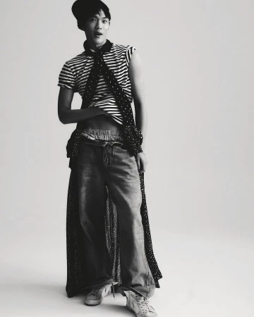 Young adult male fashion model poses in studio wearing a striped top, jeans, beanie, and polka dot scarf in a fashion editorial.