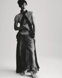 Young man wearing a striped top, dark patterned cape, and jeans against a white seamless studio background for COAT Magazine.