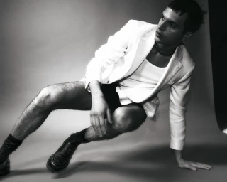 Model in a white blazer and tank top leaning against a seamless studio backdrop