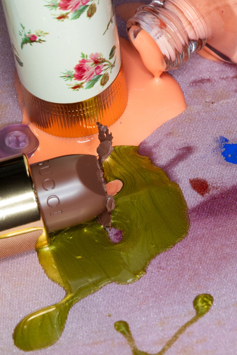 Cosmetic product bottles spilling liquids in peach, olive, and brown colors onto a textured pale purple backdrop with patterned accents.