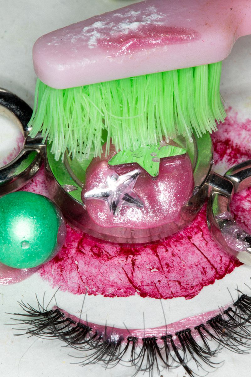 Abstract makeup still life: pink and green face makeup design with false eyelashes, brush and jewelry elements in a close-up studio shot.