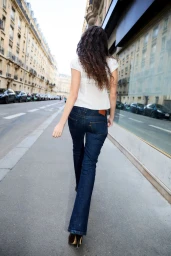 Model walking away down a city street wearing a white top and dark blue jeans