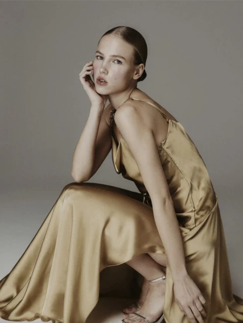 Elegant woman in a gold dress strikes a pose in a studio setting, showcasing fashion and style with a touch of sophistication.
