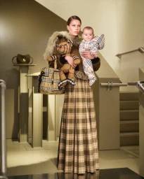 Model holding a baby and a plaid teddy bear wearing matching tartan apparel indoors on a staircase