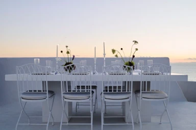 An outdoor dining table set with candles and floral centerpieces against a sunset sky and ocean view by BOSS