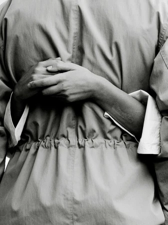 Close-up shot of a person wearing a jacket, their hands clasped behind their back, in a monochrome photo studio setting, with soft lighting.