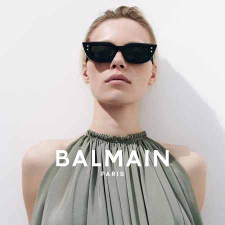 Model wearing black sunglasses and a gathered sage green halter dress against a plain white background for Balmain