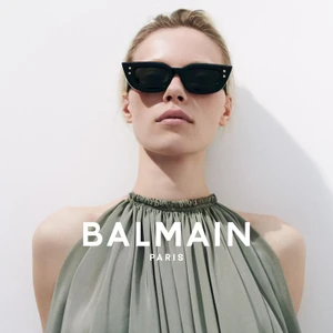 Model wearing black sunglasses and a gathered sage green halter dress against a plain white background for Balmain