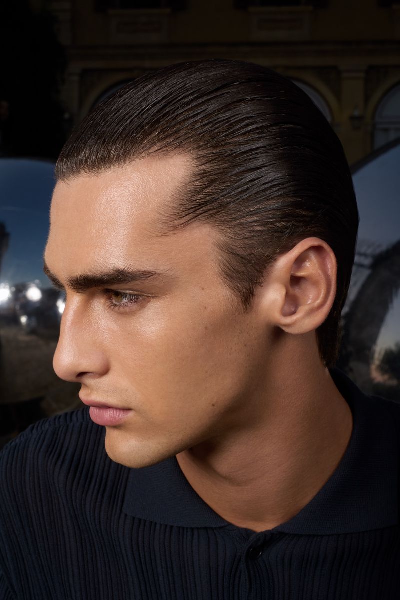 Portrait of an adult male with slicked-back dark hair, posing in a dark collared shirt, captured in an outdoor setting at nighttime.