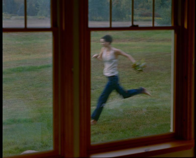 A person running across a grassy field viewed through a window frame