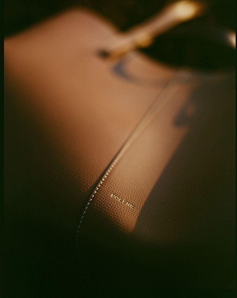 Close-up of a Polène handbag in brown leather, showing the brand's name subtly embossed with its sleek, minimalist design.