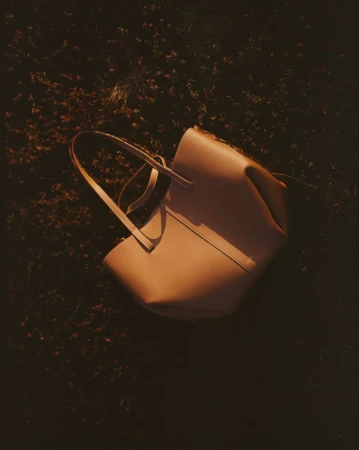 Studio shot of a stylish tan leather tote bag on a dark floral surface, bathed in warm, directional lighting.