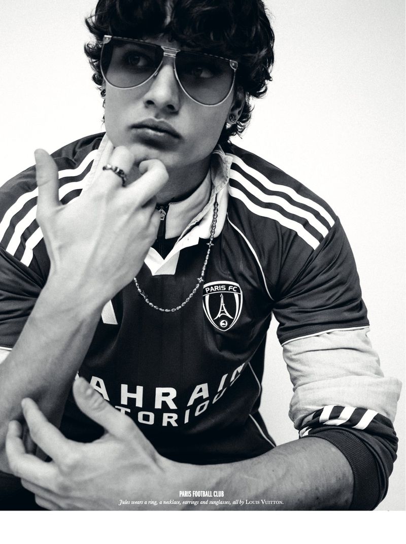 Monochrome portrait of a young man in a jersey and sunglasses, posing with his hand near his chin against a neutral backdrop.