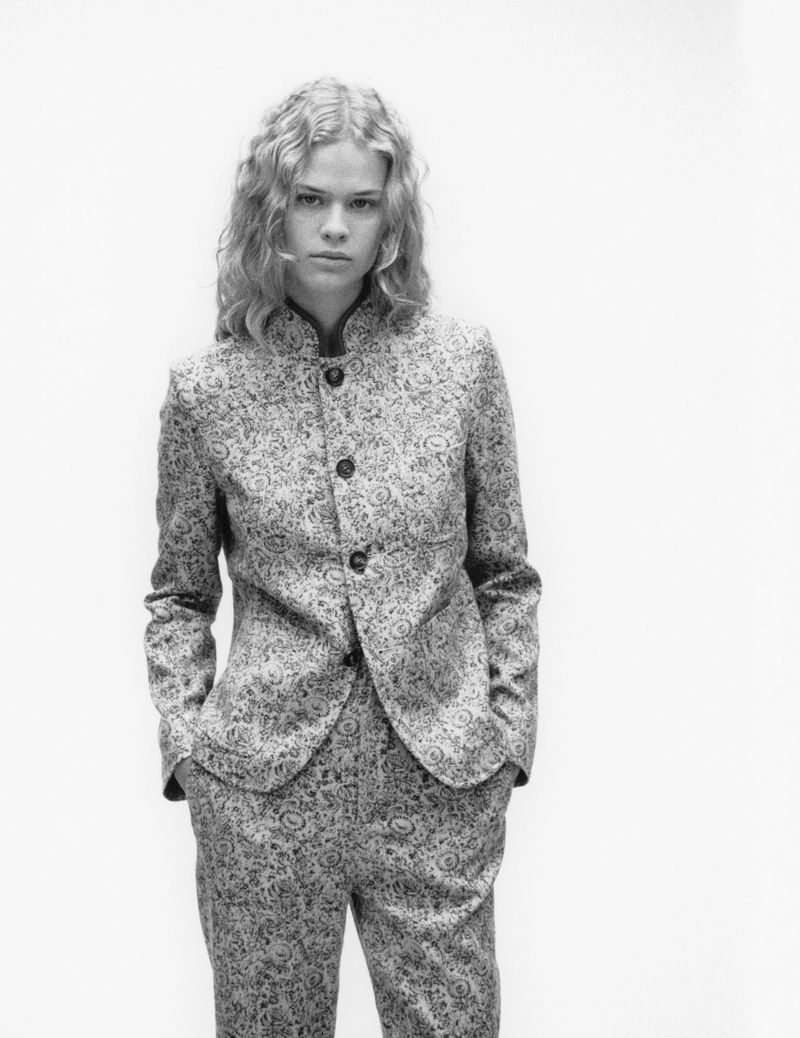 Fashionable young woman in paisley blazer and slacks poses in a studio, showcasing a modern, elegant style in black and white.