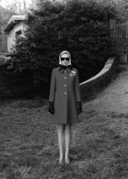 Model wearing dark sunglasses, headscarf, and a long coat standing outdoors on grass for Muse Issue 67 editorial.
