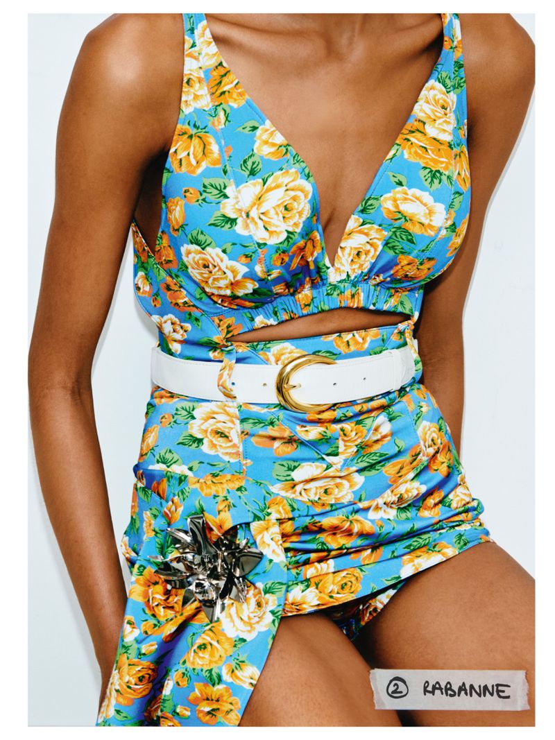 A fair-skinned person wears a blue floral crop top and skirt with a white belt featuring a gold buckle against a white backdrop.
