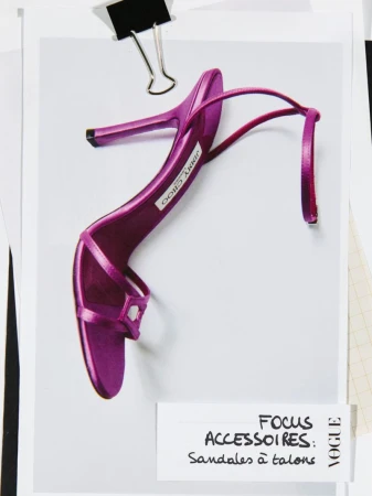 Fashion editorial image featuring a purple Jimmy Choo stiletto heel on a white surface, secured with a binder clip and surrounded by paper.