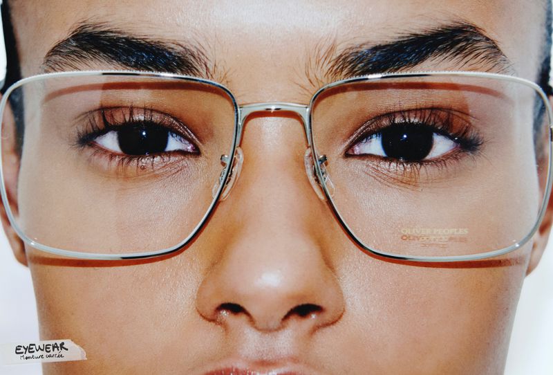 Close-up studio shot of an adult wearing rimmed glasses, highlighting eyewear design against a neutral background with natural lighting.