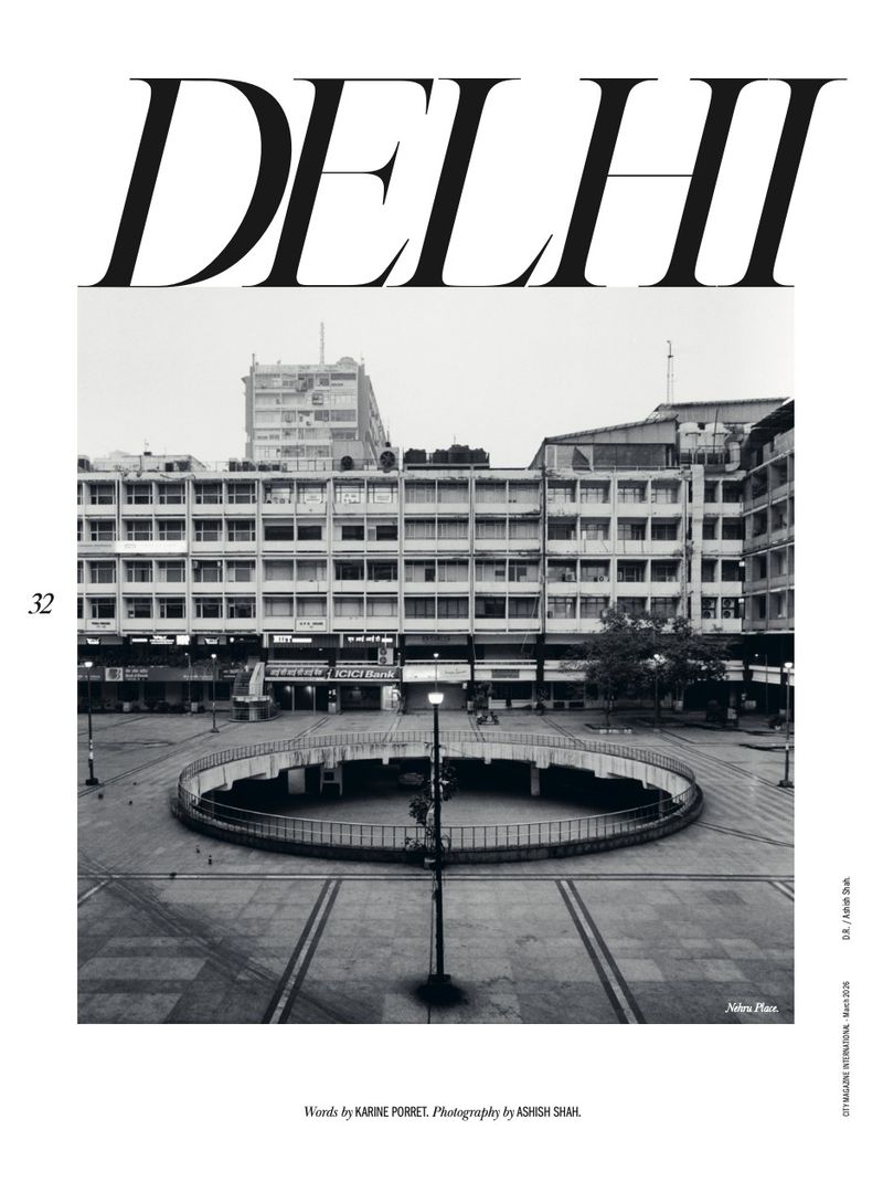 Monochrome shot of a civic plaza in Delhi, India, showcasing a circular sunken area and surrounding buildings under an overcast sky.