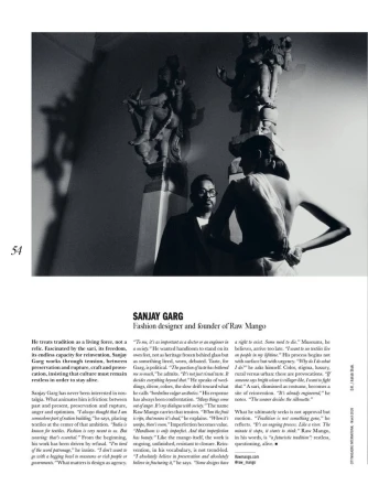 Monochrome portrait of Sanjay Garg, fashion designer, standing in front of ornate sculptures, wearing glasses and a dark suit, editorial style.
