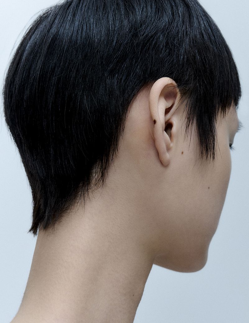 Close-up of a person with short black hair, showcasing the nape of their neck and ear against a plain light background.