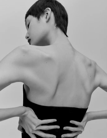 Monochrome portrait from behind of a short-haired person with hands on waist against a plain background