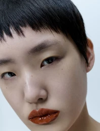 Close-up portrait of an East Asian woman with short dark hair and glossy red lipstick against a plain light background